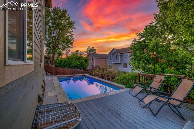 pool at dusk featuring a fenced backyard and a deck