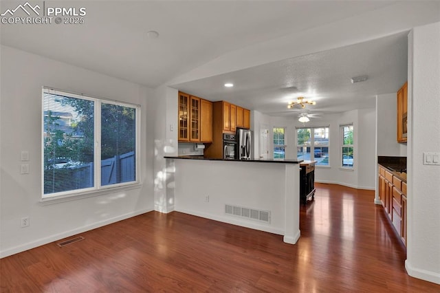 kitchen with stainless steel fridge, brown cabinets, dark wood-style flooring, dark countertops, and a peninsula