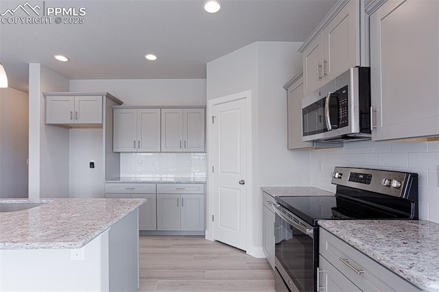 6045 Miller Run Pl, Colorado Springs, CO 80924 - kitchen featuring appliances with stainless steel finishes, light wood finished floors, gray cabinetry, decorative backsplash, and light stone countertops