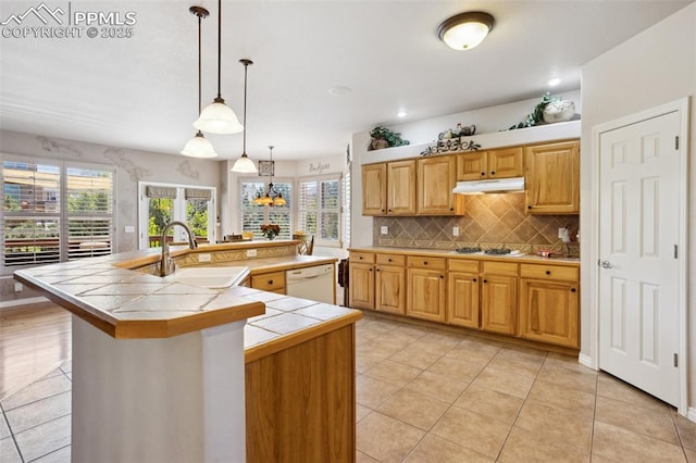 kitchen with a sink, under cabinet range hood, tile counters, white dishwasher, and gas cooktop