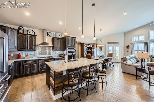 10394 Beckham St, Peyton, CO 80831 - kitchen featuring wall chimney exhaust hood, lofted ceiling, appliances with stainless steel finishes, open floor plan, and dark brown cabinetry