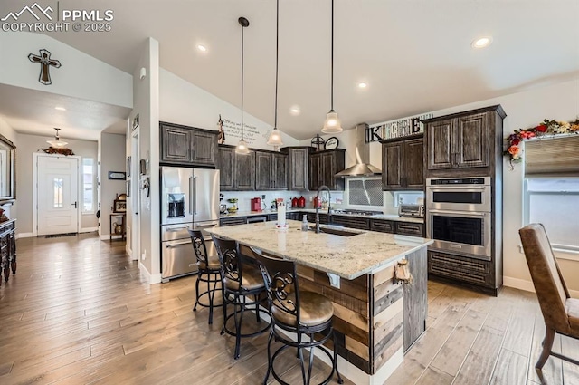 10394 Beckham St, Peyton, CO 80831 - kitchen featuring stainless steel appliances, wall chimney range hood, a sink, dark brown cabinetry, and light stone countertops