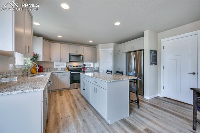 6927 Passing Sky Dr, Colorado Springs, CO 80911 - kitchen featuring appliances with stainless steel finishes, a sink, a kitchen island, light wood-style flooring, and light stone counters