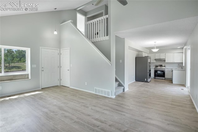 502 Fountain Mesa Rd, Fountain, CO 80817 - unfurnished living room featuring high vaulted ceiling, a sink, stairs, baseboards, and light wood-type flooring