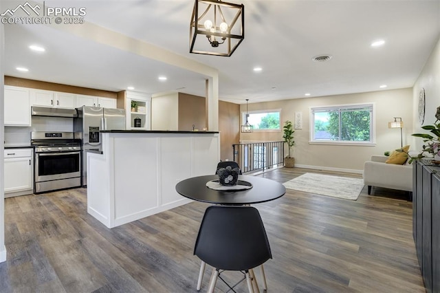 3905 Allgood Dr, Colorado Springs, CO 80911 - kitchen with appliances with stainless steel finishes, under cabinet range hood, dark countertops, a chandelier, and white cabinetry