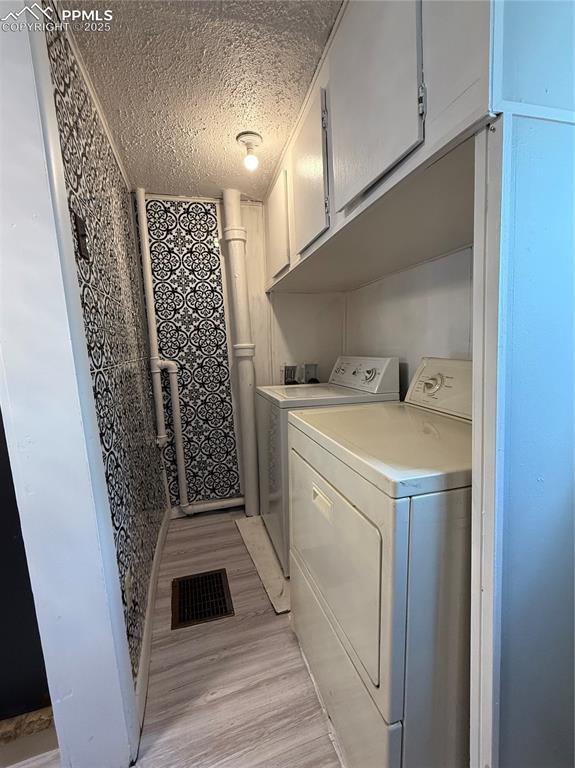 2932 W Kiowa St, Colorado Springs, CO 80904 - clothes washing area featuring washing machine and dryer, light wood finished floors, a textured ceiling, and cabinet space