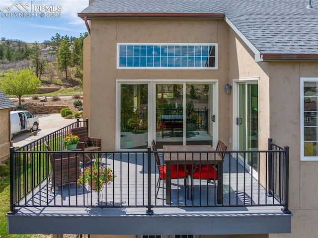 rear view of property with roof with shingles, stucco siding, and outdoor dining area