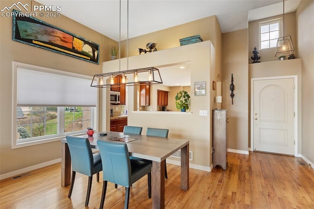 dining room featuring baseboards, light wood-style flooring, healthy amount of natural light, and a towering ceiling