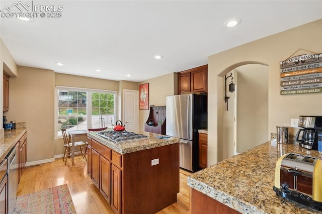kitchen featuring appliances with stainless steel finishes, light wood-style flooring, brown cabinetry, recessed lighting, and arched walkways