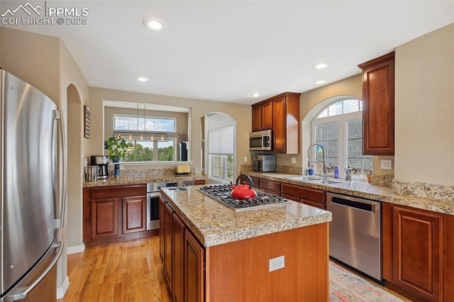 kitchen with stainless steel appliances, a sink, arched walkways, light wood-style floors, and a center island
