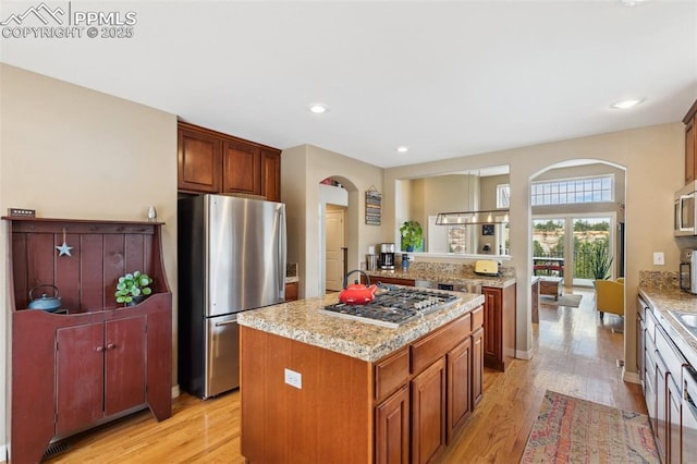 kitchen featuring appliances with stainless steel finishes, arched walkways, light wood-type flooring, and recessed lighting