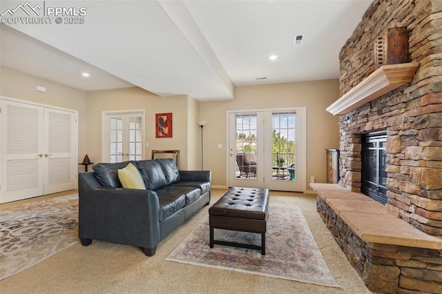 carpeted living area with french doors, a stone fireplace, and recessed lighting