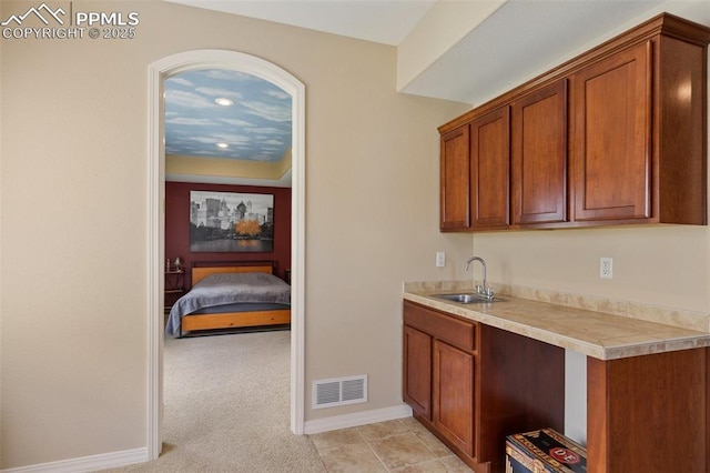 kitchen with a sink, brown cabinetry, light countertops, baseboards, and light colored carpet
