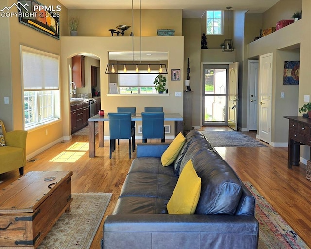 living area featuring a high ceiling, plenty of natural light, arched walkways, and light wood-style flooring