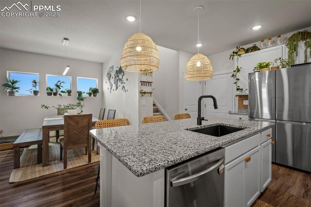 7907 Tremble Pt, Colorado Springs, CO 80908 - kitchen featuring appliances with stainless steel finishes, a sink, dark wood finished floors, a center island with sink, and white cabinetry
