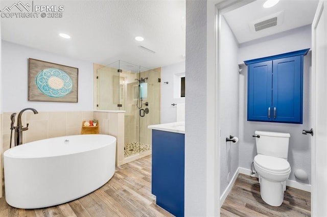 445 Wintery Cir, Colorado Springs, CO 80919 - full bathroom featuring wood finished floors, a shower stall, a freestanding tub, toilet, and tile walls