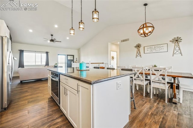 kitchen with appliances with stainless steel finishes, vaulted ceiling, a center island, dark wood-style floors, and white cabinets