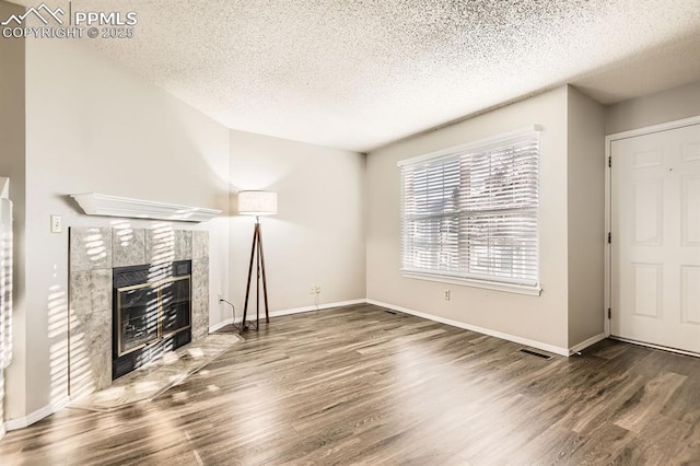 7911 Lexington Park Dr, Colorado Springs, CO 80920 - unfurnished living room featuring a textured ceiling, wood finished floors, a tiled fireplace, and baseboards