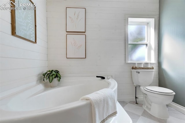 full bathroom featuring a garden tub, toilet, marble look tile flooring, wooden walls, and baseboards