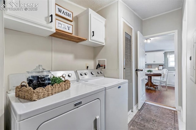clothes washing area with cabinet space, washing machine and clothes dryer, ornamental molding, a textured ceiling, and light wood-style floors