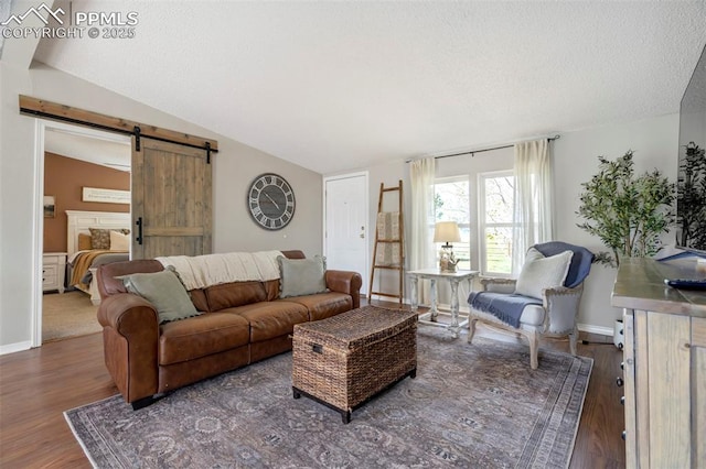 living area featuring a barn door, vaulted ceiling, wood finished floors, a textured ceiling, and baseboards