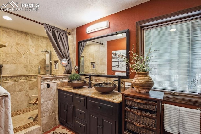 18045 Woodhaven Pl, Colorado Springs, CO 80908 - bathroom with a tile shower, double vanity, a textured ceiling, and tile walls