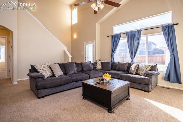 living room featuring light carpet, high vaulted ceiling, arched walkways, ceiling fan, and stairway
