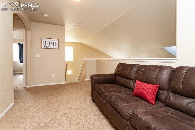 carpeted living area featuring baseboards, arched walkways, and vaulted ceiling