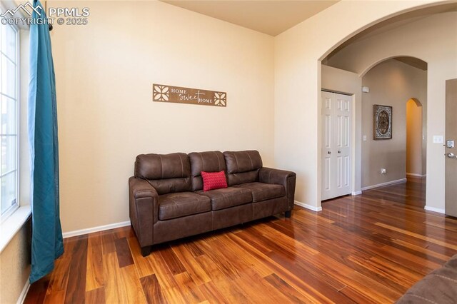 living area featuring arched walkways, wood finished floors, and baseboards