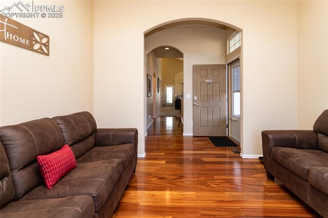 living area with arched walkways, wood finished floors, healthy amount of natural light, and baseboards