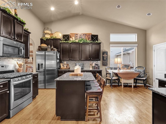 kitchen with stainless steel appliances, lofted ceiling, light stone counters, a kitchen island, and dark brown cabinetry