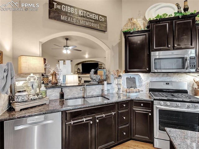 kitchen with appliances with stainless steel finishes, a sink, a ceiling fan, and dark stone counters