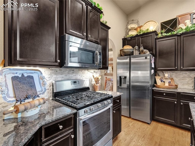 kitchen with stainless steel appliances, tasteful backsplash, dark stone countertops, arched walkways, and light wood finished floors