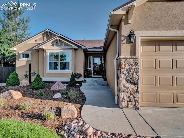 view of exterior entry featuring stucco siding, an attached garage, stone siding, and fence