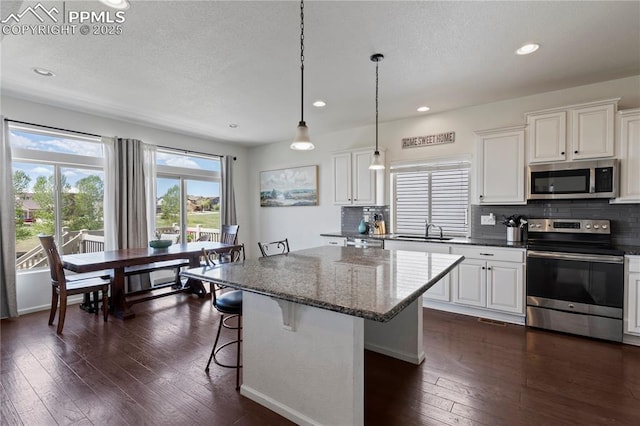 kitchen featuring stainless steel appliances, a sink, dark wood-style flooring, a kitchen island, and backsplash