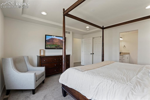 bedroom with recessed lighting, a raised ceiling, light colored carpet, and ensuite bathroom