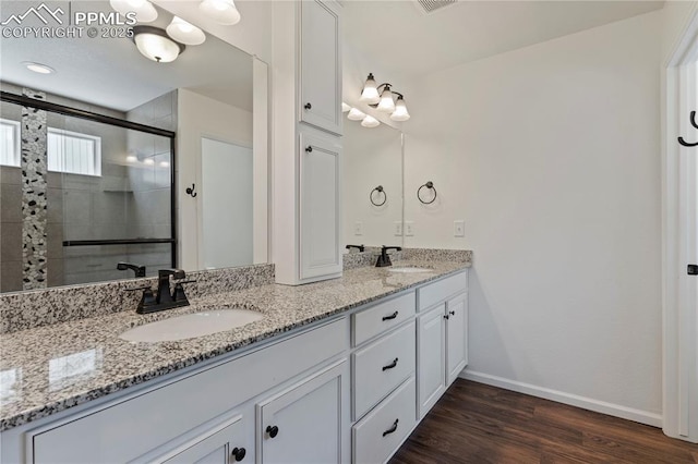 full bathroom featuring a stall shower, double vanity, wood finished floors, and baseboards