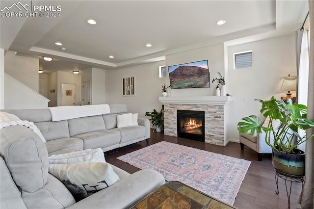 living area featuring a tray ceiling, recessed lighting, wood finished floors, a fireplace, and baseboards