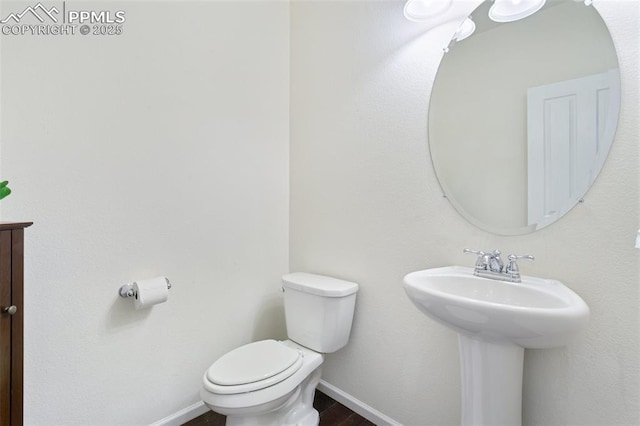 half bath with toilet, baseboards, a sink, and wood finished floors