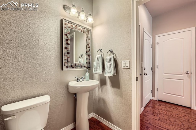 8883 White Prairie Vw, Colorado Springs, CO 80924 - half bath with wood finished floors, toilet, a textured wall, a sink, and baseboards