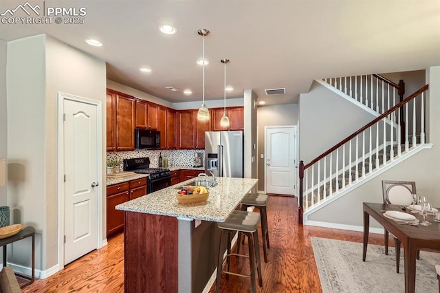 8883 White Prairie Vw, Colorado Springs, CO 80924 - kitchen with black appliances, light wood-style floors, light stone countertops, a center island with sink, and recessed lighting