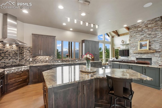 kitchen with wall chimney range hood, light wood finished floors, backsplash, light stone countertops, and recessed lighting