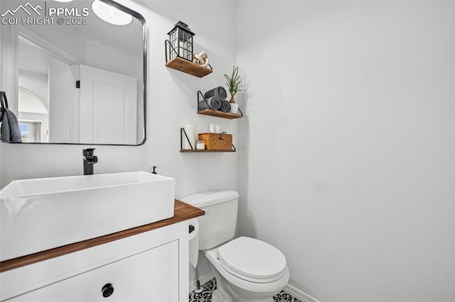 half bath with baseboards, toilet, and vanity