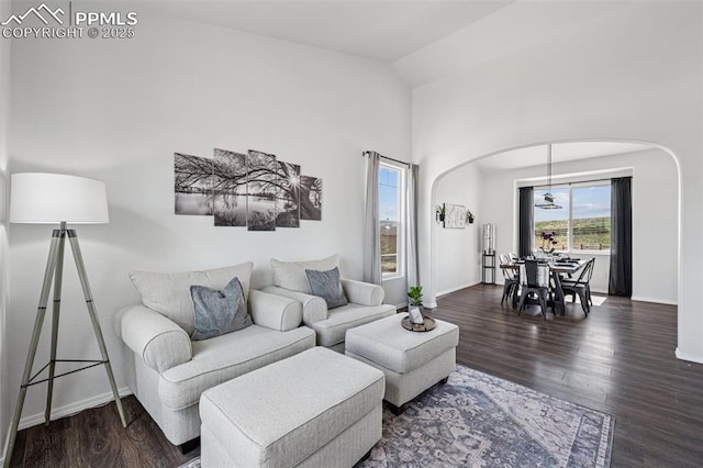 living area with arched walkways, wood finished floors, baseboards, and high vaulted ceiling