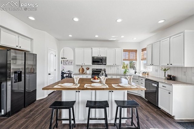 kitchen featuring appliances with stainless steel finishes, dark wood-style flooring, a kitchen island with sink, white cabinets, and recessed lighting
