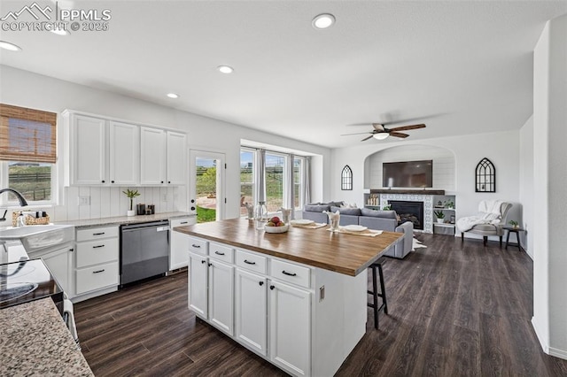 kitchen with dishwasher, wooden counters, a glass covered fireplace, ceiling fan, and white cabinets
