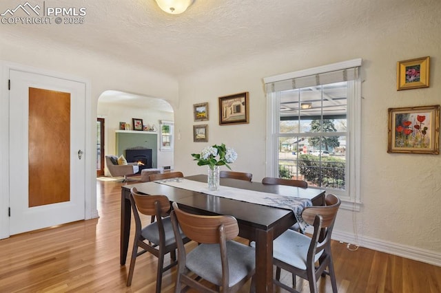 1003 N Institute St, Colorado Springs, CO 80903 - dining area with arched walkways, wood finished floors, a lit fireplace, a textured ceiling, and baseboards