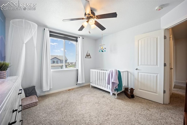 carpeted bedroom with a crib, a textured ceiling, and ceiling fan