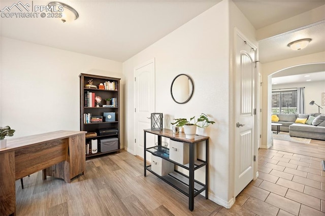 home office with arched walkways, baseboards, and wood finished floors