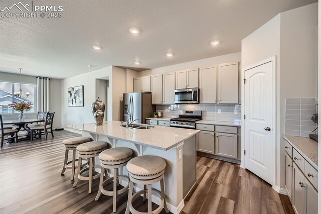 10737 Rolling Mesa Dr, Falcon, CO 80831 - kitchen with appliances with stainless steel finishes, dark wood-style floors, a sink, a kitchen bar, and decorative backsplash